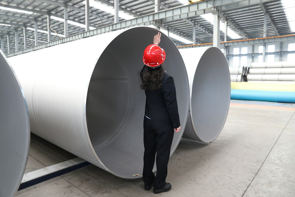 A worker inspecting large metal pipes on a factory floor