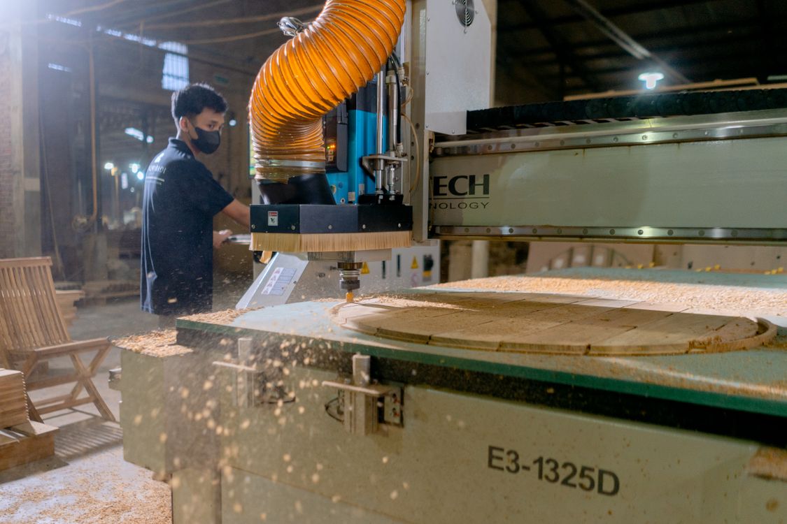 A CNC router cutting a wooden furniture panel while an operator monitors production